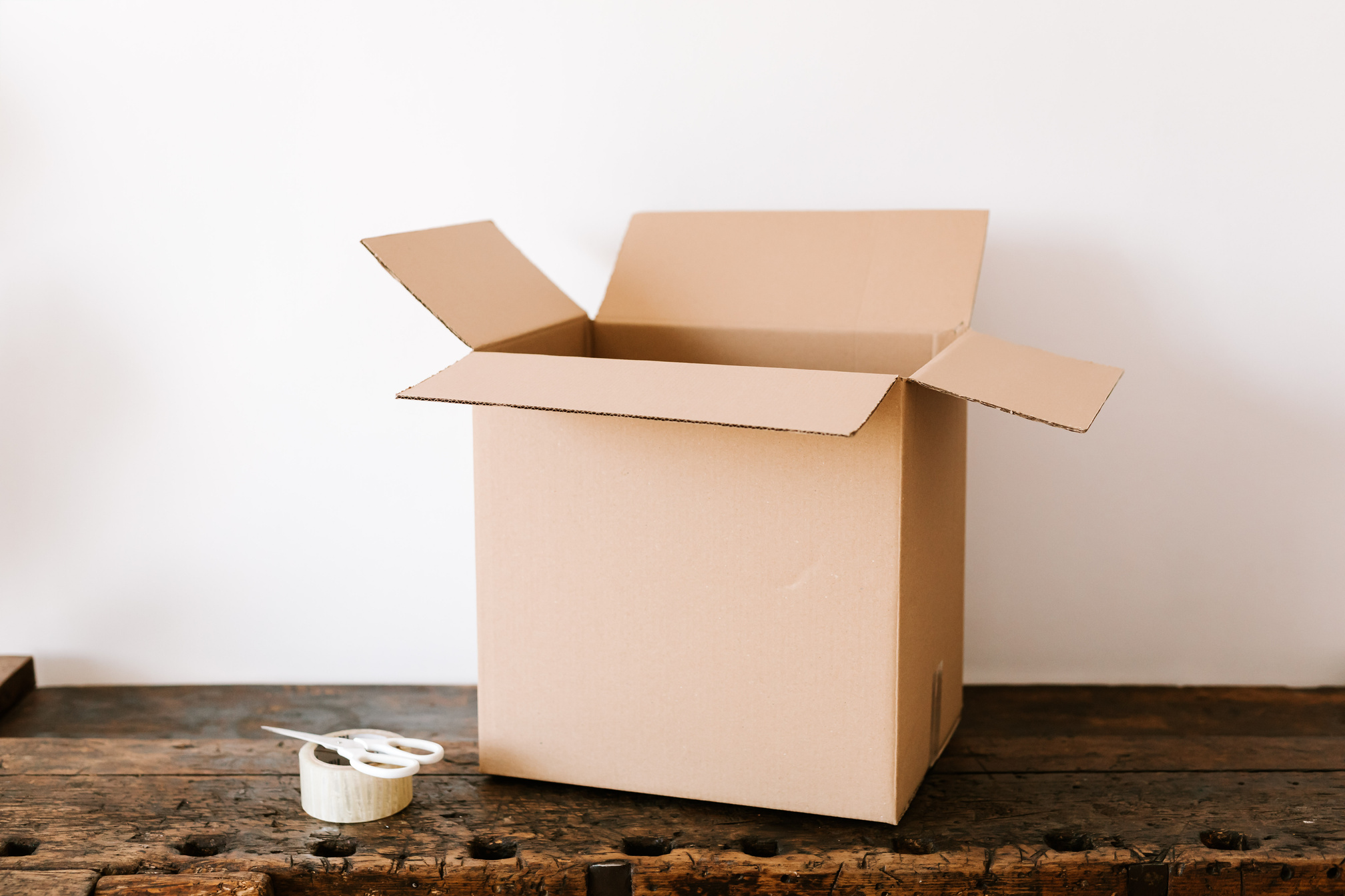 Cardboard box on dark wooden table near tape and scissors