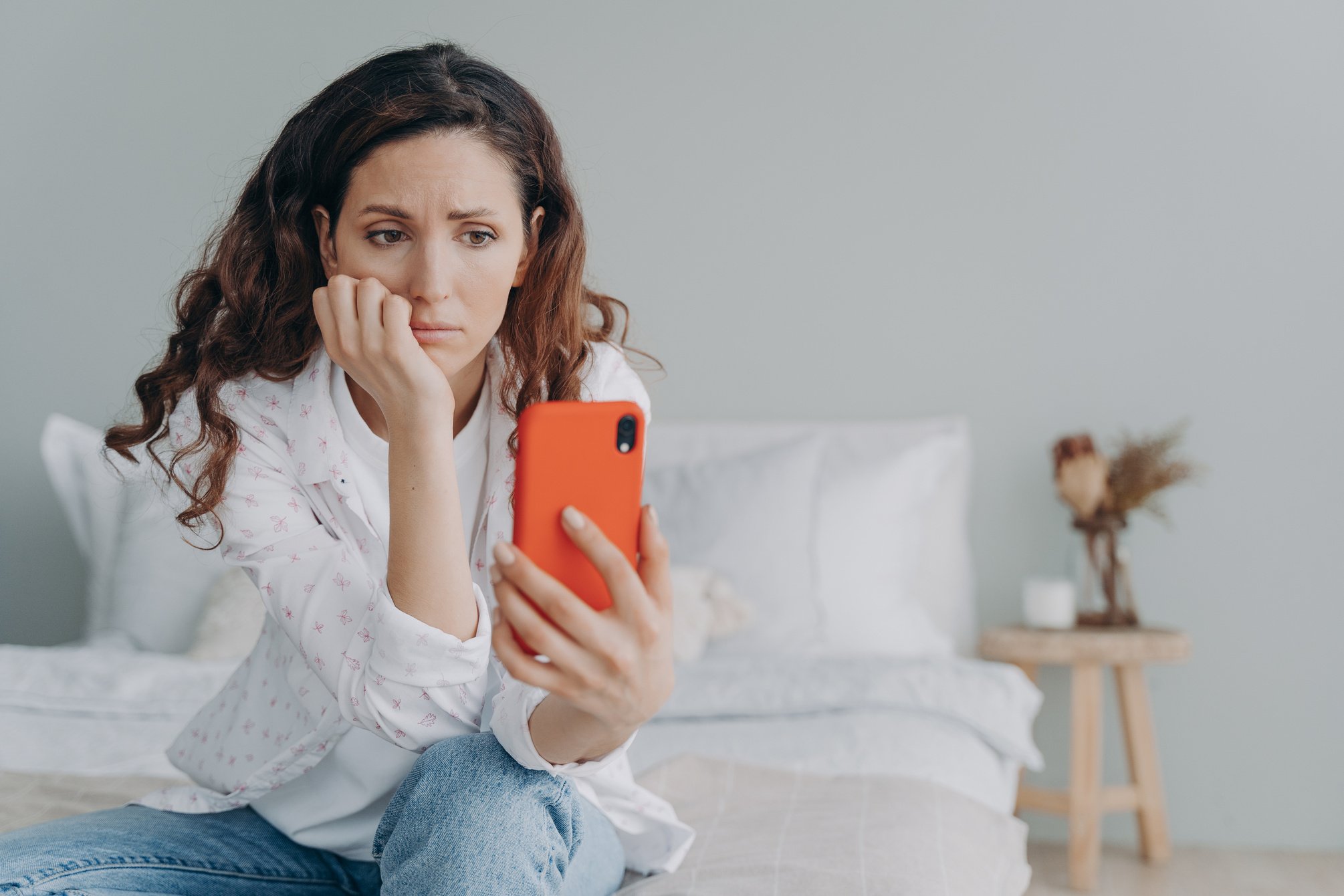 Stressed caucasian woman is doom scrolling. Girl reading morning news on smartphone in her bedroom.